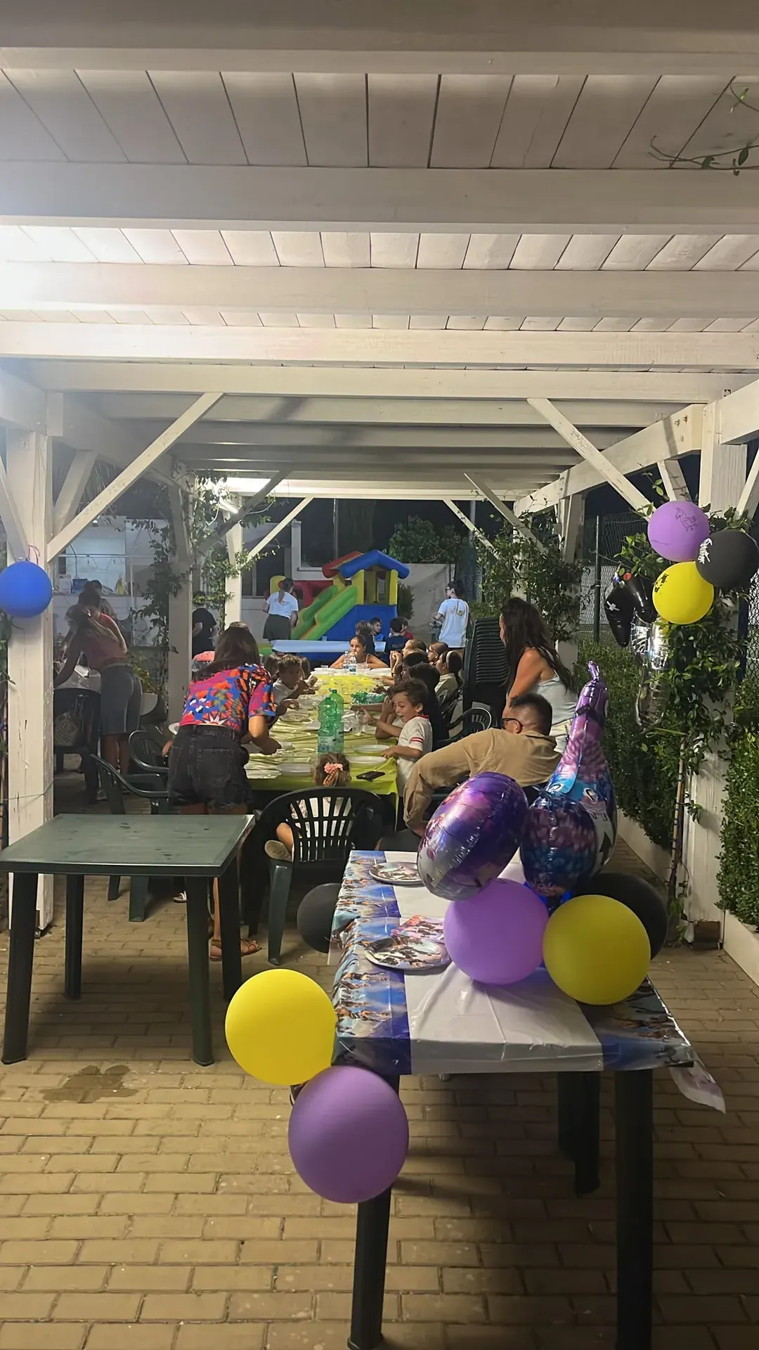 Festa di compleanno per bambini sotto il pergolato, con tavolata e palloncini viola e gialli